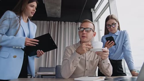 Office team cooperation at work. Man drinking coffee and talking to female colleagues.