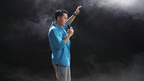 Side View Of Asian Man Holding A Microphone And Rapping On The Black Background