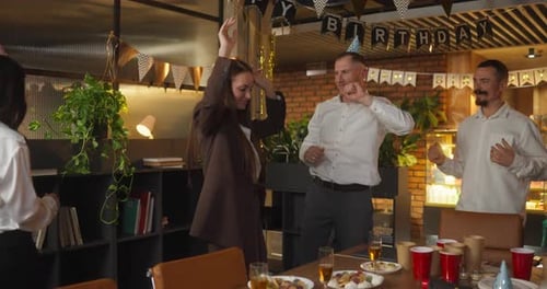 A Group of Cheerful Office Workers in Business Suits Dance Near the Festive Table During a Corporate