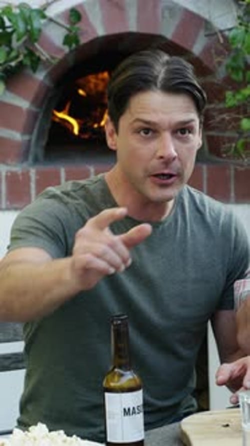 Man Drinking Beer and Pointing Near a Brick Oven