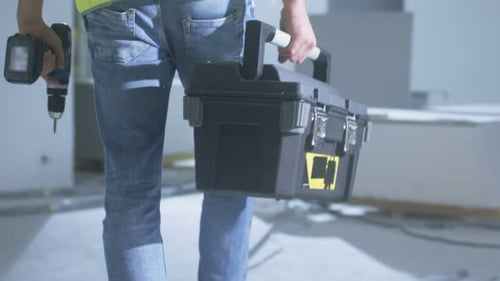 Construction Worker Walking inside Building Under Construction and Carrying Toolbox