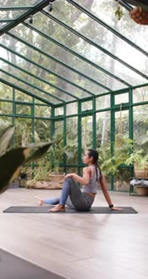 Vidéo verticale : Pratiquant le yoga, femme effectuant une pose de bridge sur un tapis dans une maison en verre