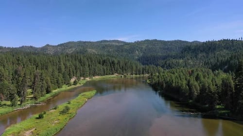 4K Drone pushes in over a wide mouthed river as it flows. There is thick dense green forest that cas