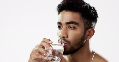 Mann trinkt Wasser, Flüssigkeitszufuhr und Gesundheit mit ernstem Gesicht und Glas in der Hand isoliert auf weißem Grund