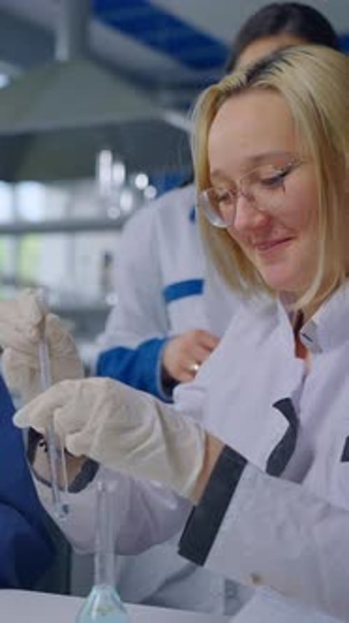 Female Laboratory Researchers Conducting Chemical Experiment with Test Tubes and Protective Gloves