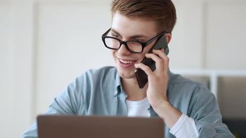 Young Adult Talking on Phone While Using Laptop