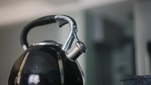 Black Metal Kettle Boiling with Steam on a Gas Stove in a Modern Kitchen Close Up of Dark Teapot