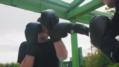 Young Caucasian Boxer Taking Rapid Jabs in Outdoor Sparring Under Green Frame Quick Footwork Gloves