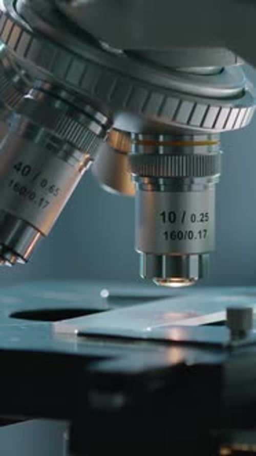 Hand of Lab Technician Adjusting Specimen Table and Ocular of Microscope