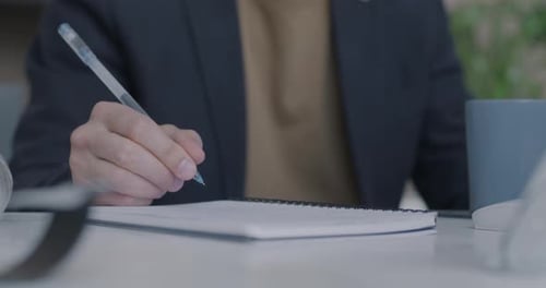 Closeup of Male Hand Writing in Notebook While Businessman Planning Work at Desk in Office