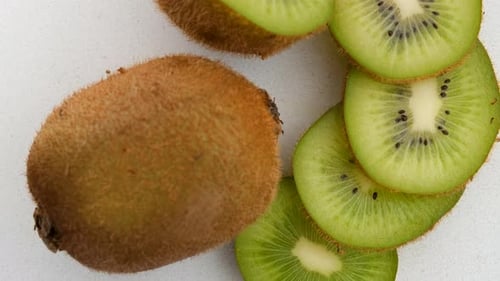 Close Up Top View Of Whole And Sliced Kiwi Rotating Clockwise And On A Marble Surface