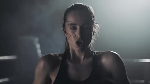 Determined Woman Shouts in Dark Boxing Ring