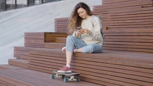 Young Woman Using Phone, Sitting with Skateboard