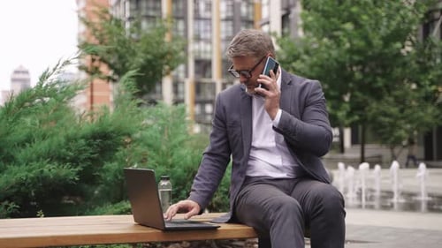 Adult Man Working on Laptop and Talking on Smartphone in the City Real Time Concept