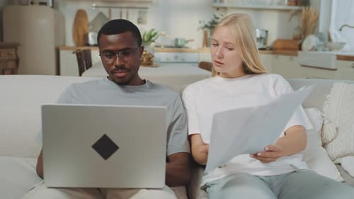 Man and Woman Look at Papers with Laptop