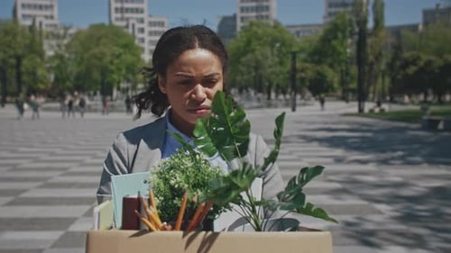 Unemployed Woman Carries Box of Office Supplies in Outdoor Park