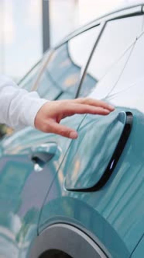 Nahaufnahme männlicher Hände, die ein Ladekabel an ein Elektrofahrzeug auf einem Parkplatz im Freien anschließen