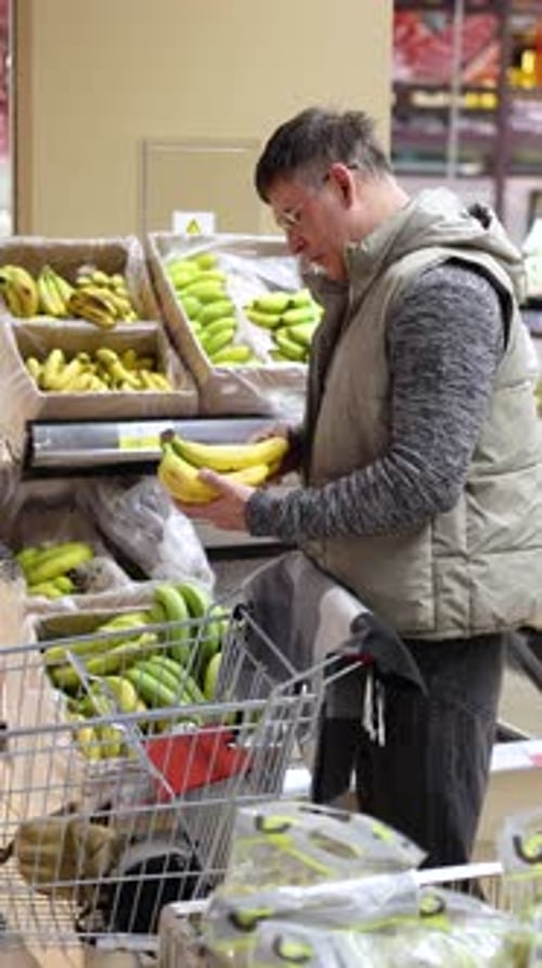 Vertical Video of a Man Picking Bananas From a Supermarket Counter and Adding Them to His Basket