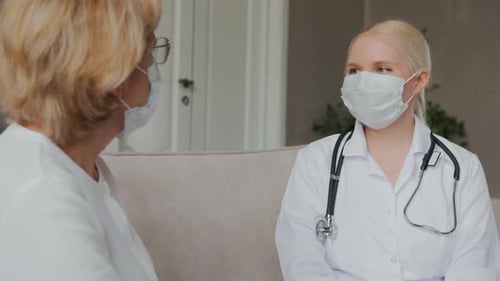 Doctor Talking to Senior Patient in Home Wearing Masks