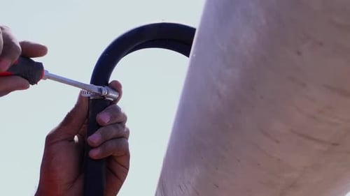 View Of Screwdriver Being Used To Tighten Hose Clamp On Pipe Outside. Low Angle