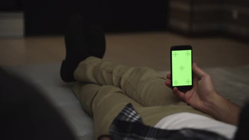 Man Lying on Couch Using Smartphone with Chroma Key Green Screen at Night