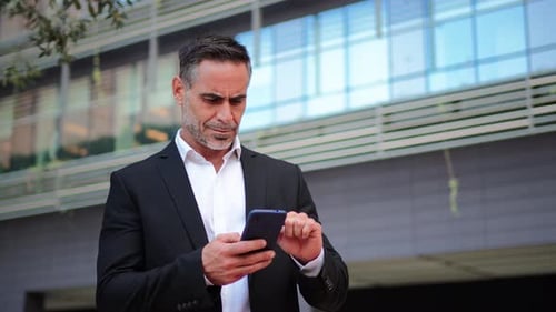 Man in Suit Using Smartphone Outside Building