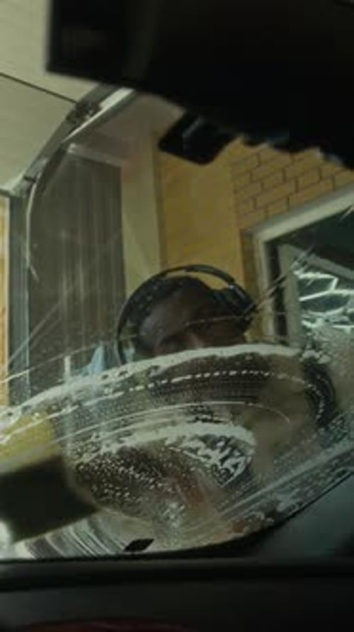 Vertical of Black Man Washing Car Windshield with Sponge and Soapy Water