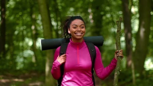 Smiling African American Woman Hiking in Green Forest Carrying Yoga Mat and Walking Stick