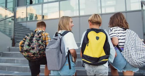 Rear view. Good-looking school child friends climb stairs going to class with backpacks. Boys girls