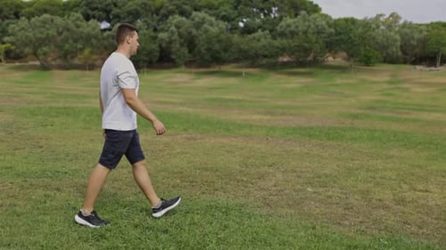 Young Man Walking Across a Green Grassy Park