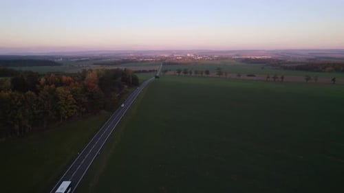 Blick auf vorbeifahrende Autos und einen Bus auf der Straße, die zur Stadt führt, bei Sonnenuntergang im Herbst