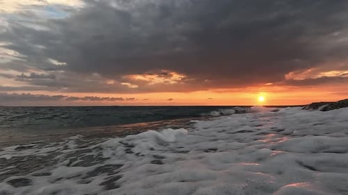 Gros plan à angle bas des vagues s'échouant sur une plage de galets lors d'un coucher de soleil majestueux. Photo sur trépied.