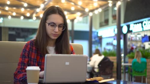 A Young Woman is Working on a Laptop in a Cafe