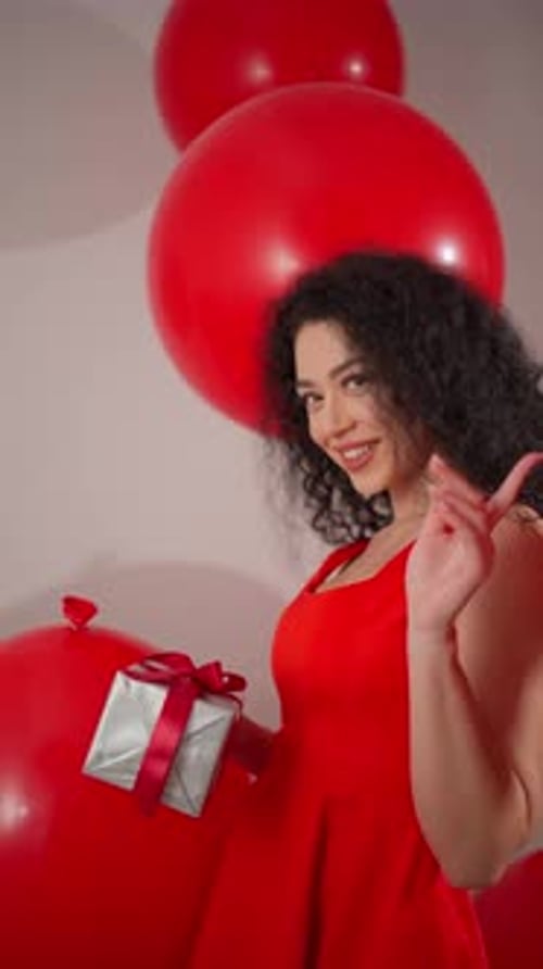 Woman Holding Gift Surrounded by Festive Red Balloons