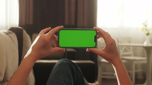 Woman Lying on Sofa in Cozy Living Room Watching Smart Phone Green Screenclose Up on Female Hands