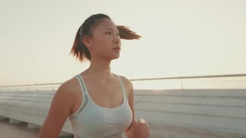 Asian girl in sports top runs along the promenade at morning time