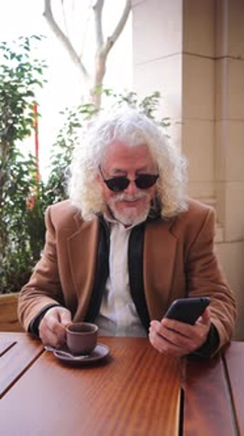 Senior Man Using Phone at Outdoor Cafe Table