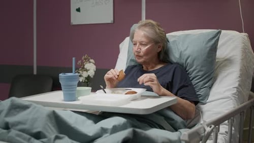 Mature Female Patient Eating Meal while Resting in Hospital Bed
