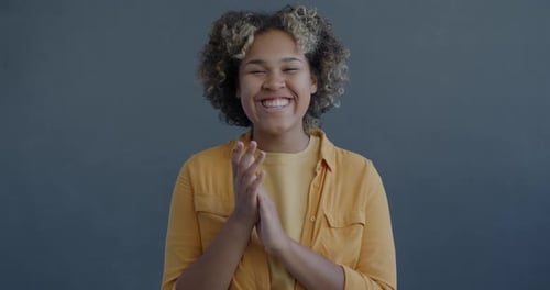 Smiling Woman Clapping in Front of a Gray Background