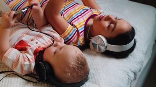 Children Listen to Music on Headphones Lying on Bed