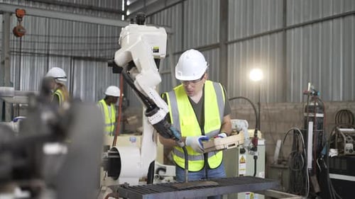 Blue collar workers at machine shop with welding robot arm.