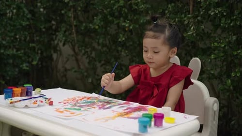 happy toddler girl painting watercolor in a paper at backyard