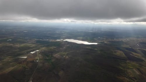 Aerial view, Flying over green fields at level of cumulus clouds with sun rays, fly into gray cloud