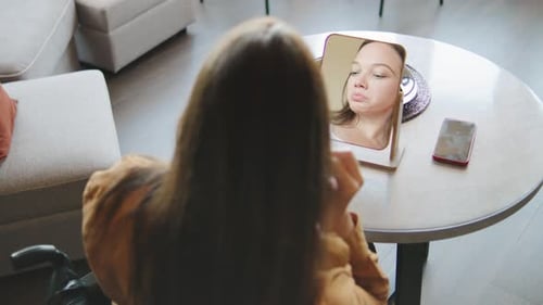 Young Woman Puts On Earrings Looking in Mirror