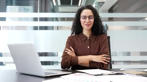 Portrait of smiling female financier sitting at desk at workplace in modern business office. Happy