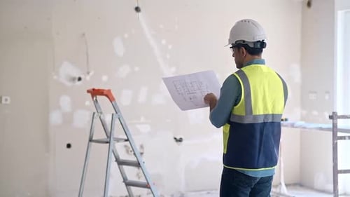 Specialist Examining Interior Project Drawing Stands Against Construction Equipment
