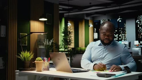 Afroamerikanischer Büroangestellter legt zur Erinnerung eine Haftnotiz auf seinen Laptop