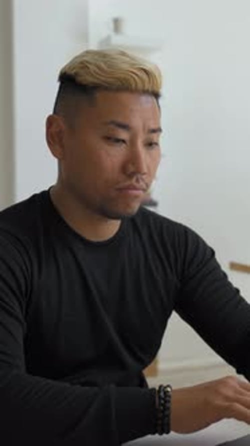 Vertical of Asian Man Works Online on Laptop Sitting at Office Desk