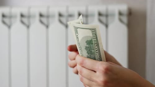 Person Counting Stack of Money in Front of Radiator