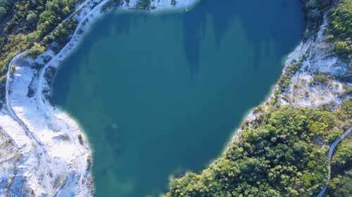 Aerial View From Above of a Turquoise Lake in an Old Quarry Surrounded By a Road Houses and Trees